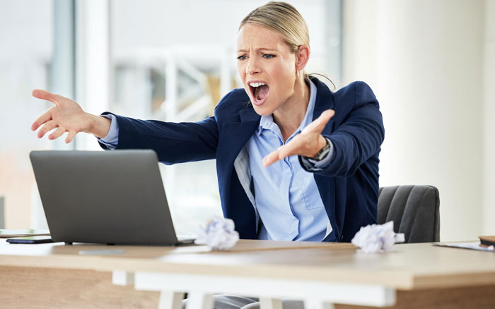 Office coordinator frustrated at laptop, reacting to pushy colleague testing limits in a busy office setting.