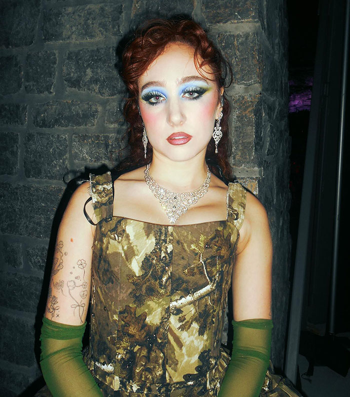 Chappell Roan wearing a vintage-style dress and bold makeup, posing against a stone wall after Grammys look outrage.
