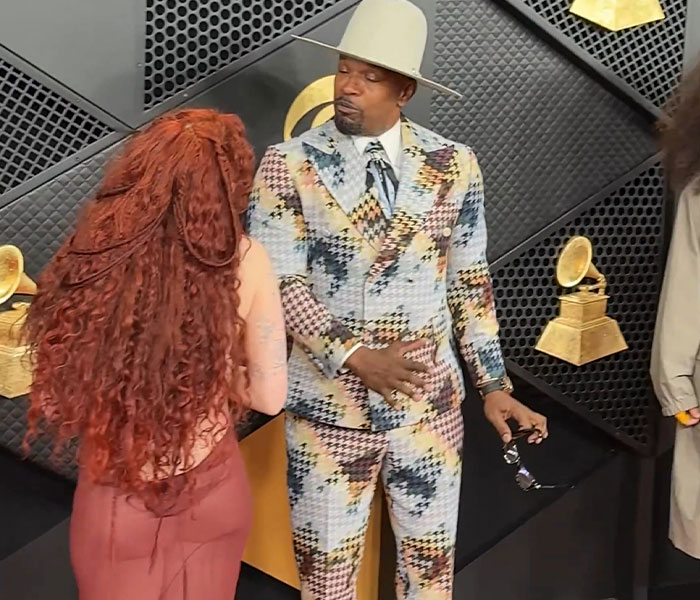 Man in colorful suit and hat making awkward celebrity reaction at the 2026 Grammy Awards red carpet event.