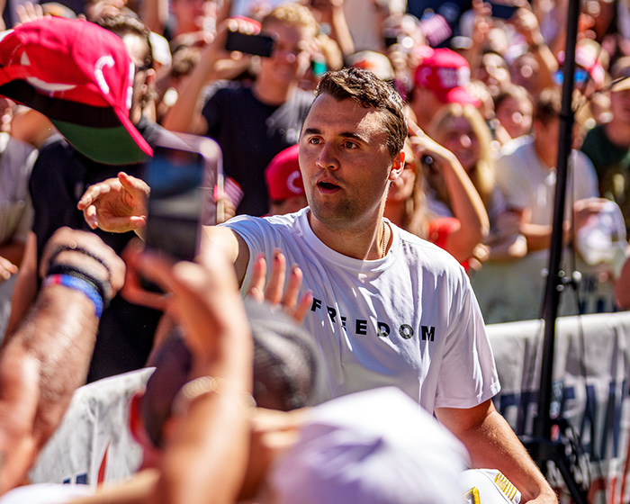 Man wearing a freedom shirt engaging with crowd, representing themes of Candace Owens and police questioning Erika Kirk.