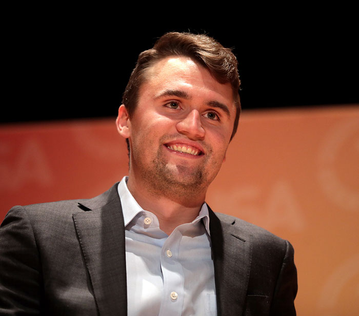 Young man in a dark suit smiling during a public event, related to Erika Kirk's relationship with Charlie scrutiny.