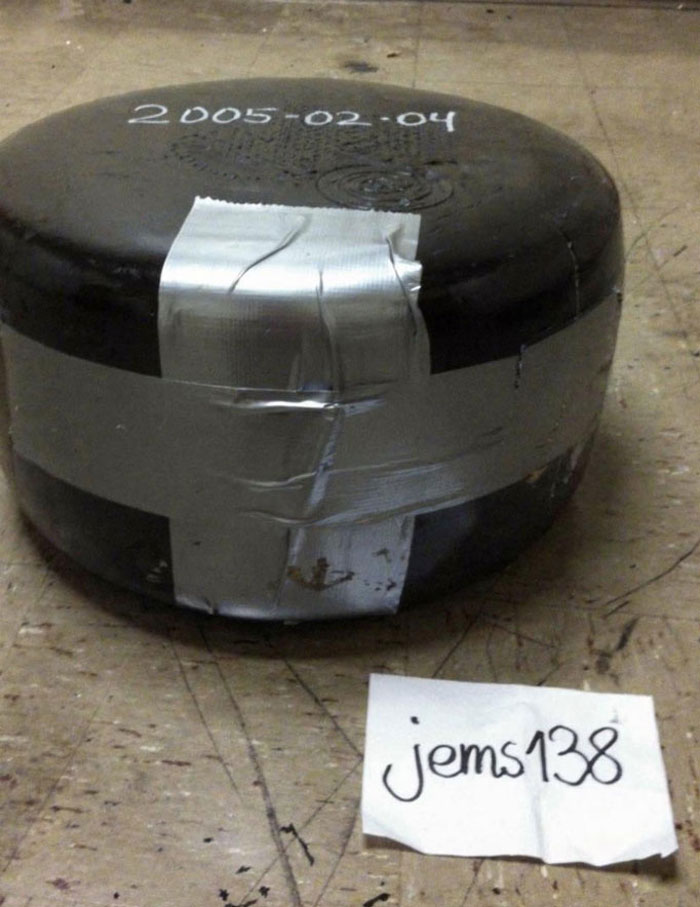 Large cheese wheel wrapped with duct tape on a worn floor, labeled with a date, relating to cheese wheel girlfriend relationship.