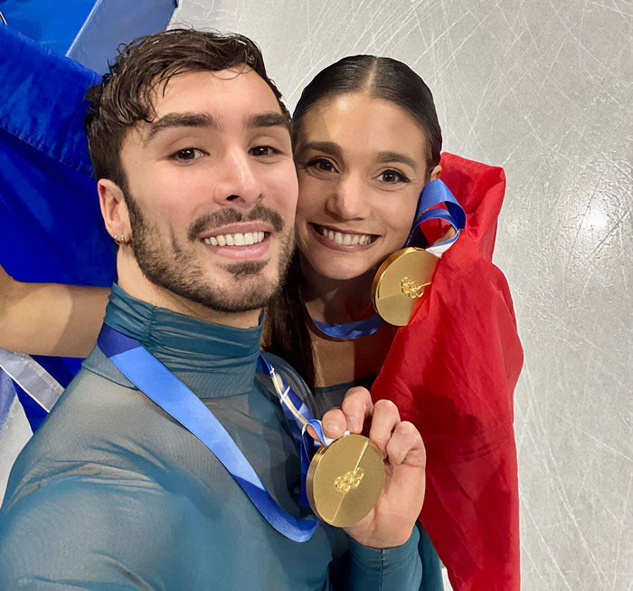 French ice skaters posing with gold medals on ice after Olympic event amid cheating scandal controversy.