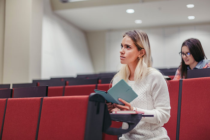 Colorblind student attentively reading notes in a lecture hall, highlighting the challenges faced with special needs support.
