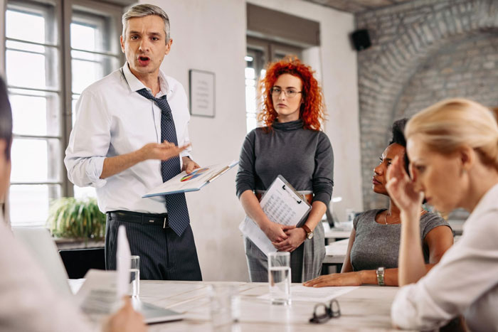 Man discussing with colleagues in an office while a woman in casual clothes listens during a professional meeting.