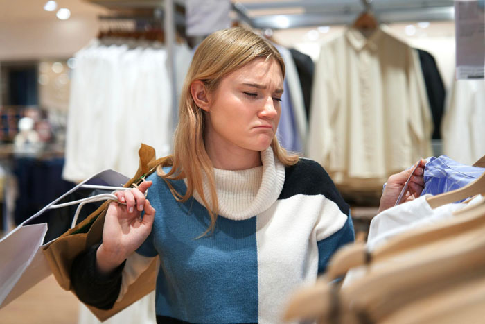 Young woman in a store looking unsure while holding clothes, representing frumpy clothes as protection from harassment.