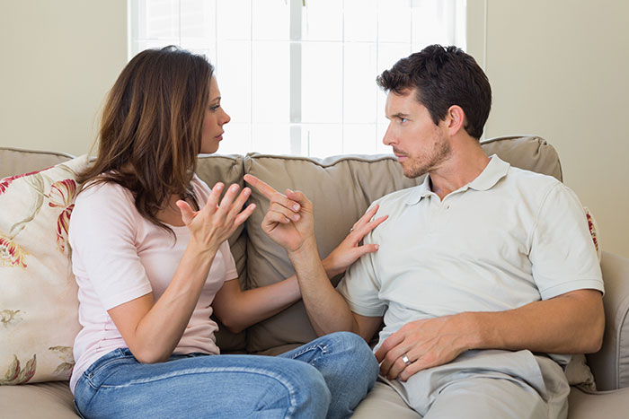 Couple having relationship drama on a couch with the boyfriend reacting to girlfriend wishing he was more manly.
