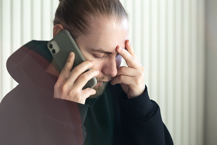 Young man on phone looking stressed, illustrating relationship drama involving manly traits and boyfriend clapping back.