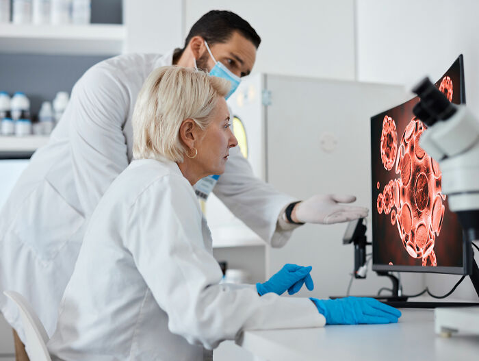 Two scientists in lab coats analyzing colon cancer cells on a computer screen during medical research breakthrough.