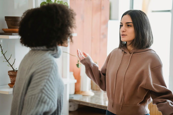 Two women having a serious conversation indoors, illustrating cousin card fraud risks in vacation rental situations.