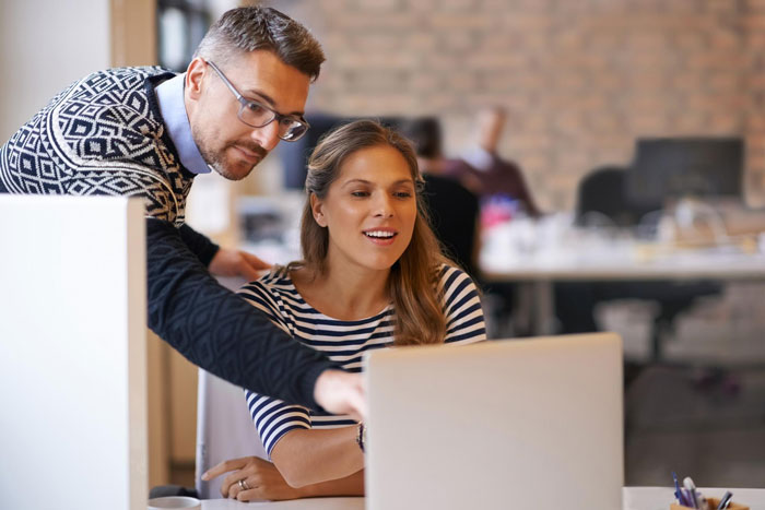 Two coworkers collaborating at a laptop in a modern office, illustrating coworker reported HR gets fired situation. Two coworkers collaborating at a laptop in a modern office, illustrating coworker reported HR gets fired situation.
