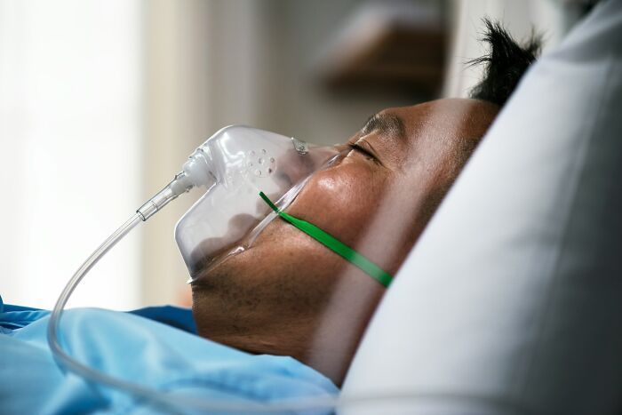 Patient lying in hospital bed wearing oxygen mask, illustrating dangerous things often dismissed by people.