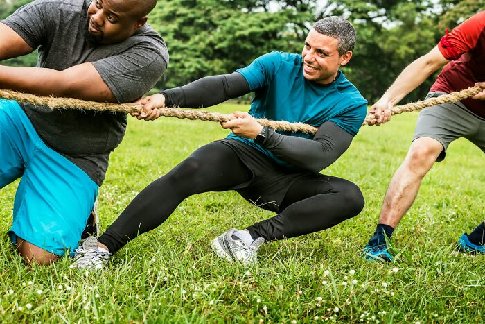 Three men competing in a tug of war outdoors, showcasing the strength and intensity of Olympic sports competition.