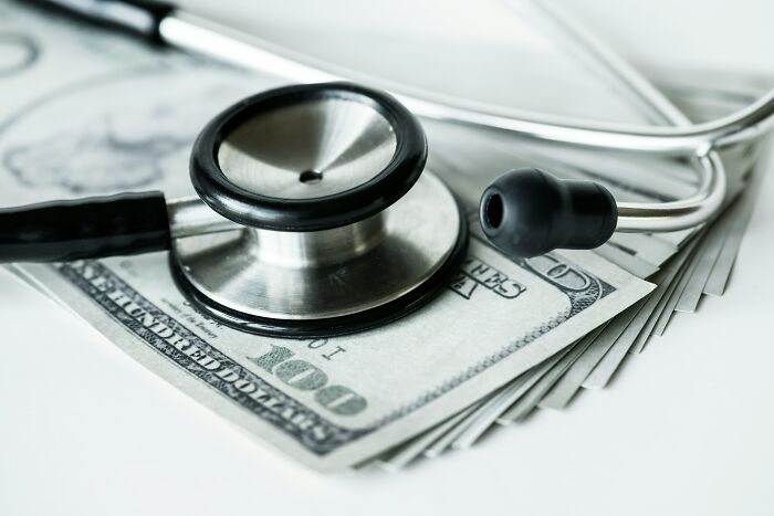 Stethoscope resting on a stack of hundred-dollar bills symbolizing medical expenses and financial struggles.