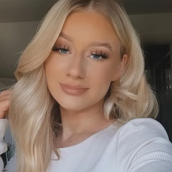 Blonde young woman with long eyelashes and light makeup, posing indoors related to legal expert explaining case.