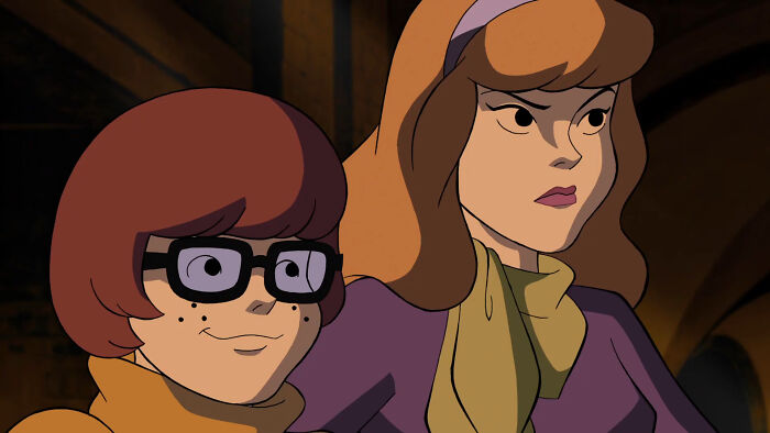 Animated Scooby Doo characters Velma and Daphne in a dark setting, highlighting Scooby Doo fans rallying for Velma.