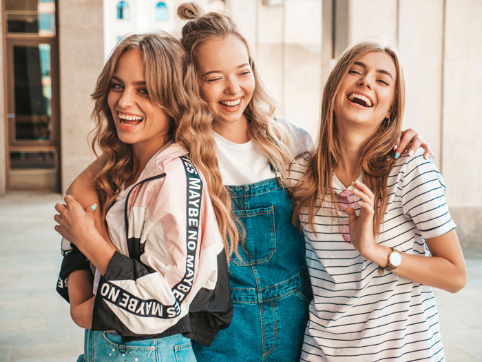 Three teenage girls smiling and hugging outdoors, capturing moments before a sleepover with creepy vibes from a friend's dad.