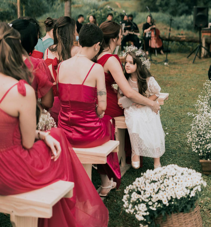 Guests in red dresses at an outdoor wedding with a flower girl in white, capturing a 20k wedding and reactions a year later.
