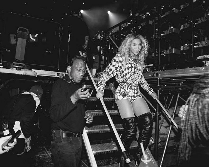 Beyoncé backstage walking down stairs in patterned outfit with staff, highlighting treatment of 20-year employee debate.