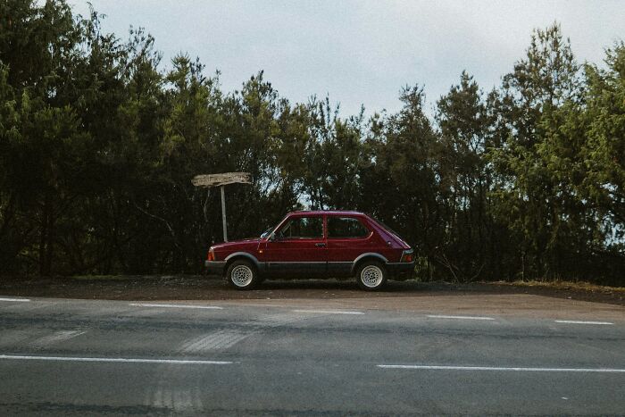 Red car parked by an empty roadside with dense green trees, symbolizing friendships ended without even starting.