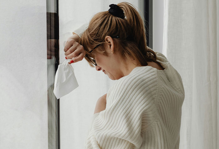 Woman holding tissue by window, emotional and crying, representing a wife seeking a second chance from her husband.