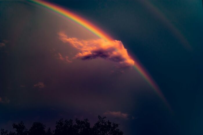 Vivid rainbow with dark clouds at dusk, evoking strange things witnessed that made people question everything.