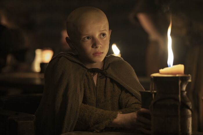 Young boy known as Egg, a key Aegon Targaryen character, sitting by candlelight in a dim medieval setting.
