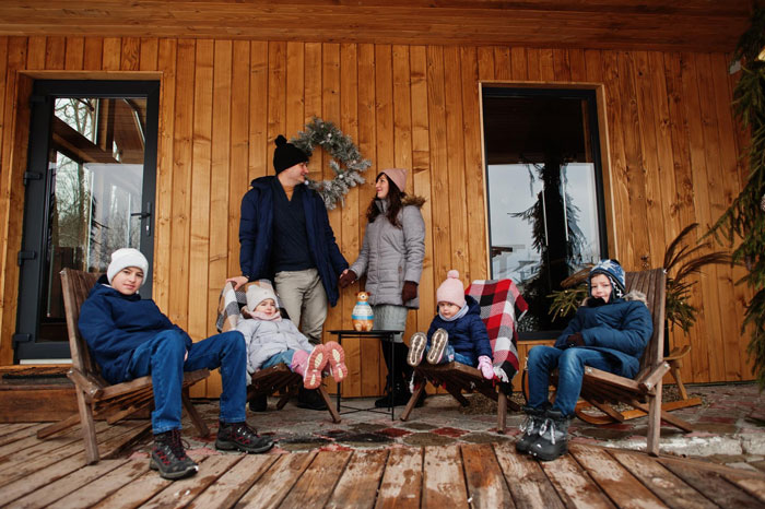 Family with three toddlers outside a tiny cabin dressed for winter, capturing a birthday with outdoor activities and cozy moments.