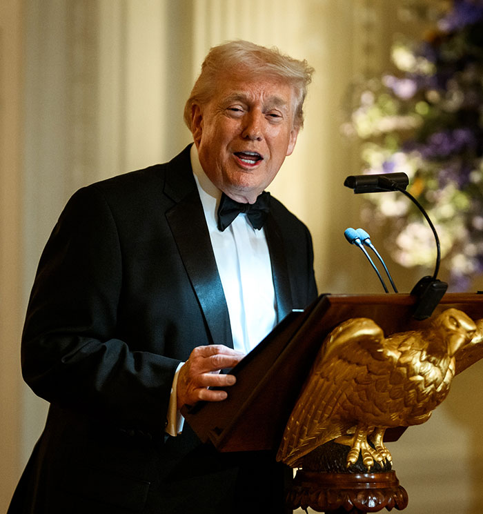Man in a tuxedo speaking at a podium with a golden eagle, related to US Olympics hero Jack Hughes breaking silence. Man in a tuxedo speaking at a podium with a golden eagle, related to US Olympics hero Jack Hughes breaking silence.