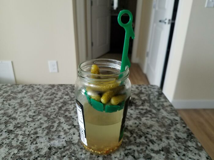 Small green tool lifting pickles out of glass jar, showcasing interesting tools that solve annoying little problems.