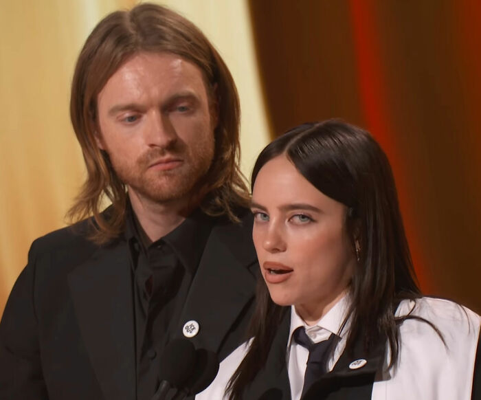 Billie Eilish speaking at the Grammys with a focused expression, highlighting her anti-ICE message.