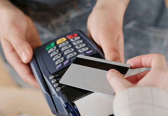 Person holding a card near a payment terminal, illustrating criminals shockingly bad at what they do with card transactions.