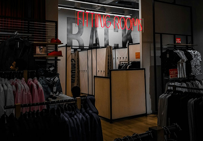Clothing store fitting rooms with racks of clothes and a neon sign, illustrating criminals bad at what they do.