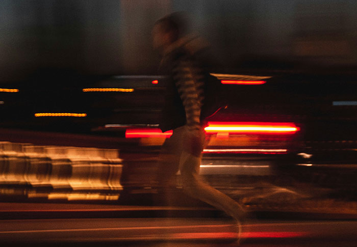 Blurred image of a person running at night with streaks of red and yellow lights in the background, showing criminals bad at crimes.
