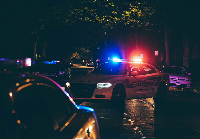 Police car with flashing lights on a dark street at night, related to criminals shockingly bad at what they do.