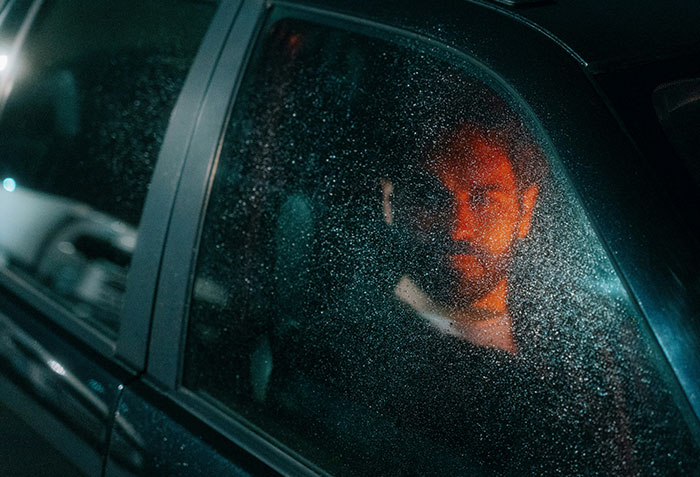 A man with a serious expression sitting inside a car at night, illustrating criminals shockingly bad at what they do.