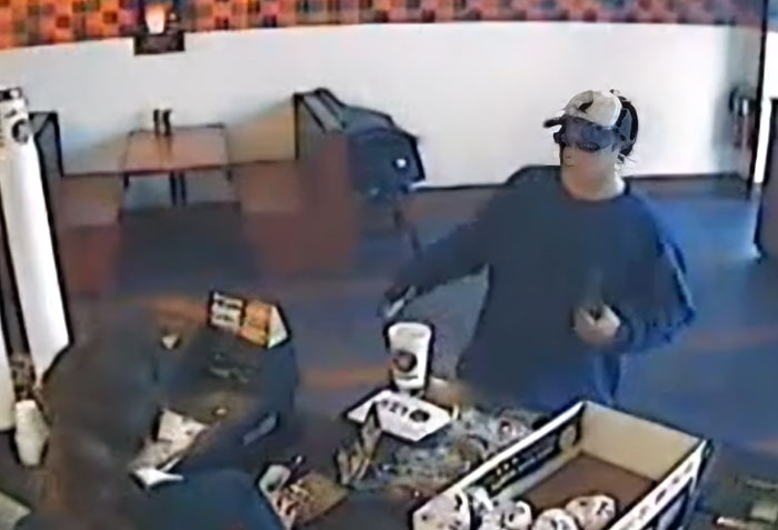Surveillance image showing a criminal in a baseball cap attempting a robbery, illustrating criminals shockingly bad at what they do.