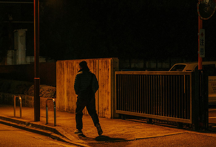 Person walking alone at night near a fence and dimly lit street, illustrating criminals shockingly bad at what they do.