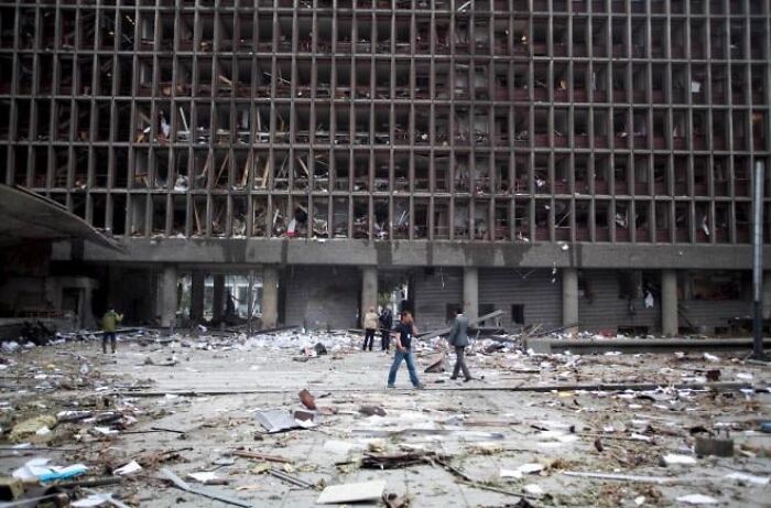 People walking through debris and destruction in front of a ruined building, evoking a dystopian nightmare scene.