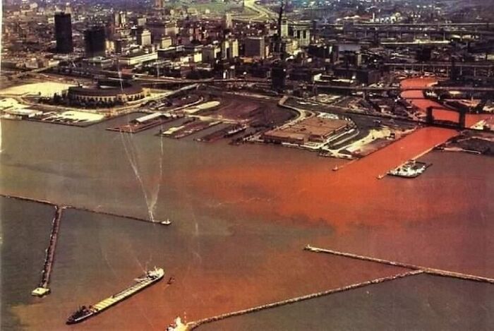Aerial view of an industrial harbor with polluted reddish-brown water, evoking a dystopian nightmare scene.