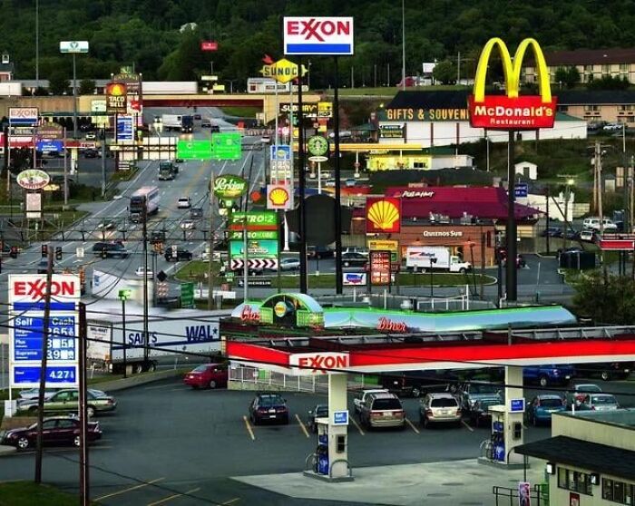 Dystopian nightmare scene of a congested urban street filled with gas stations, fast food signs, and heavy commercial clutter.