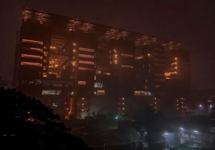Dimly lit dystopian building glowing through thick fog, creating a haunting and nightmarish urban atmosphere.