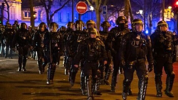 Riot police in full gear marching at night, creating a dystopian nightmare scene in an urban environment.