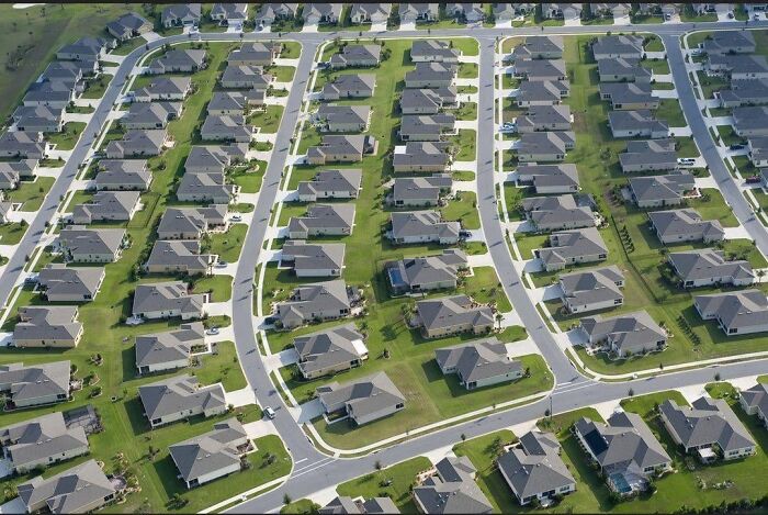 Aerial view of a sprawling suburban neighborhood with repetitive houses and streets resembling a dystopian nightmare.