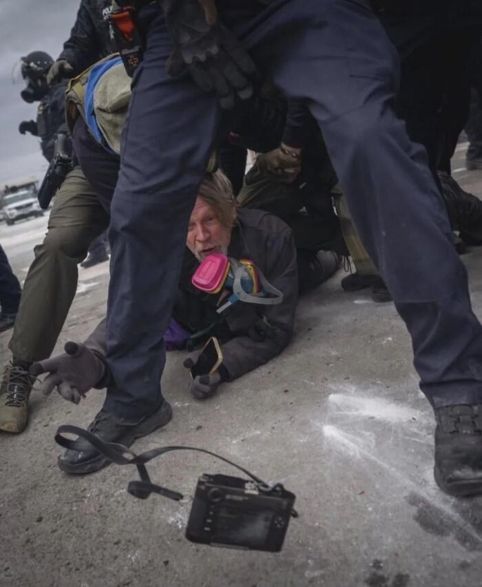 Police detaining a protester wearing a gas mask on the ground, captured in a horrifying dystopian nightmare scene.
