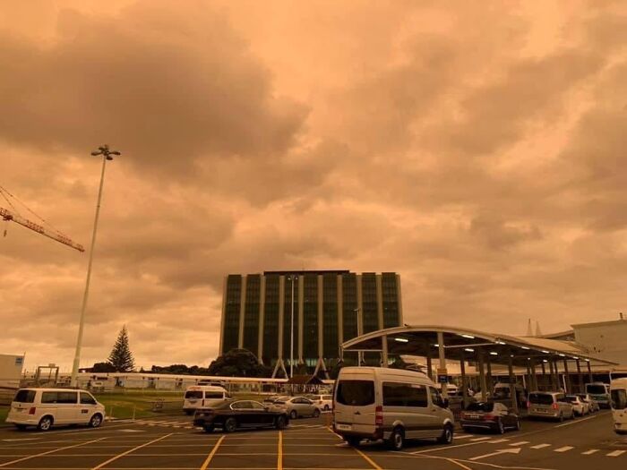 Dystopian nightmare sky over a parking lot with vans and dark clouds above a modern office building.