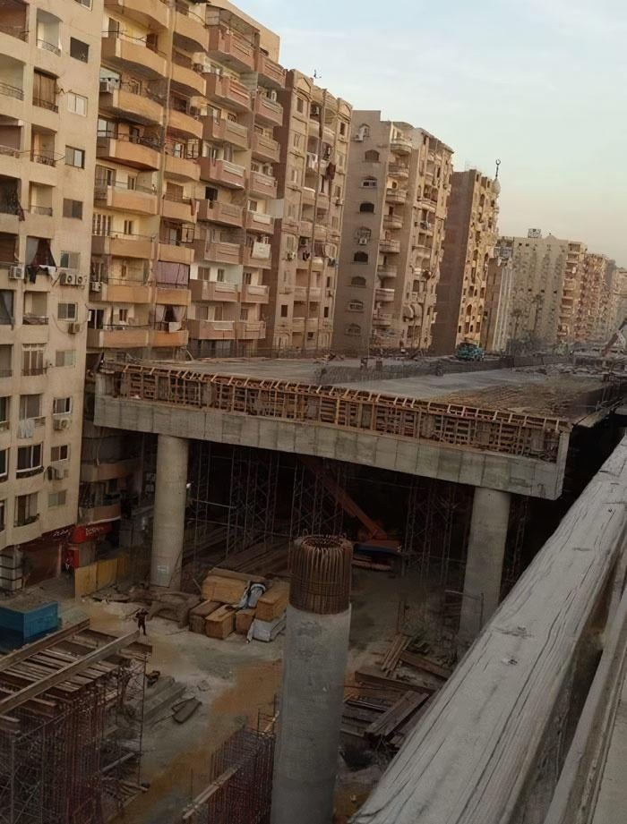 Dystopian nightmare scene of unfinished construction surrounded by worn apartment buildings in an urban environment.