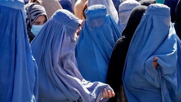 Women wearing blue burqas in a crowded outdoor setting, evoking a dystopian nightmare atmosphere from around the world.
