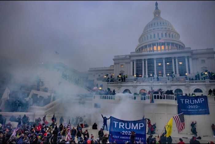 Crowd outside US Capitol with smoke and protest banners, creating a dystopian nightmare scene.