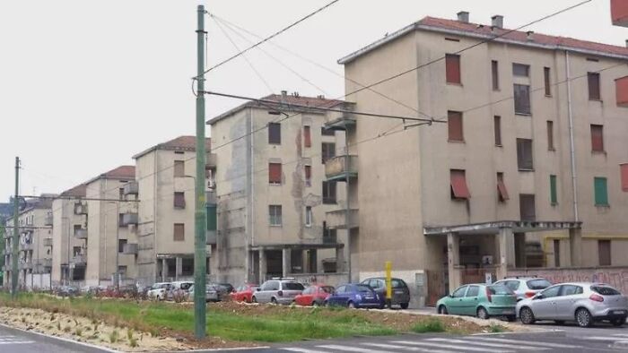 Dystopian nightmare scene of deteriorating apartment buildings with abandoned cars parked along an empty, neglected street.
